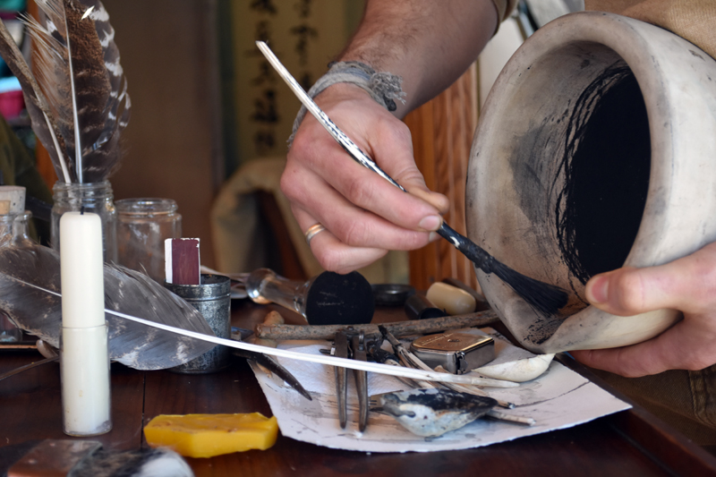 Somerville artist Nathan Allard empties charcoal made from animal bones into a seashell to be mixed into egg tempera paint. The brush is made with a feather from the right wing of a bird to fit over Allard's right hand. (Elizabeth Walztoni photo)