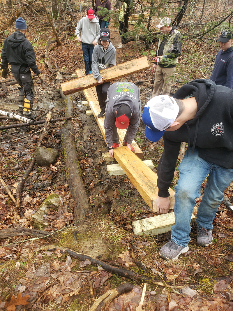 Eighth grade students at the Great Salt Bay School assemble a bridge on the school trail with help from Coastal Rivers staff and a volunteer. (Photo courtesy Coastal Rivers Conservation Trust)