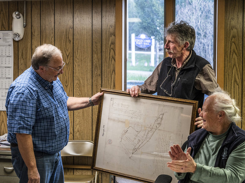 Outgoing Edgecomb Select Board member Ted Hugger (left) receives a framed 1795 map of the town from Chair Mike Smith as new board member Fran Mague applauds on Tuesday, April 18. (Bisi Cameron Yee photo)