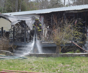 A Whitefield firefighter sprays down a hot spot on the deck outside of a home onTownhouse Road in Whitefield Saturday, April 29. (Sherwood Olin photo)