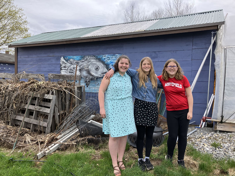 From left: Whitefield Elementary School seventh graders Bristol Jewett, Stella Martinelli, and Audrey Tibbetts, stand outside the small greenhouse, getting excited to see their seedlings being sold at the seedling sale Friday, May 19 and Saturday, May 20. (Meira Bienstock photo)