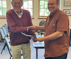 Bill Brewer (left) shakes hands with Damariscotta Select Board Chair Daryl Fraser on Wednesday, June 7, holding the town report dedicated to Brewer that evening. While he declined to give a speech, Brewer said he was surprised by the announcement. (Photo courtesy Rebecca Bartolotta)