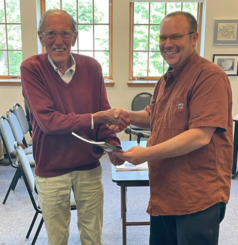 Bill Brewer (left) shakes hands with Damariscotta Select Board Chair Daryl Fraser on Wednesday, June 7, holding the town report dedicated to Brewer that evening. While he declined to give a speech, Brewer said he was surprised by the announcement. (Photo courtesy Rebecca Bartolotta)