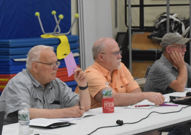 From left: Dresden Select Board members John Rzasa, Donald Gleason Jr., and Allan Moeller vote on an article during the annual town meeting at Dresden Elementary School on Tuesday, June 20. (Meira Bienstock photo)