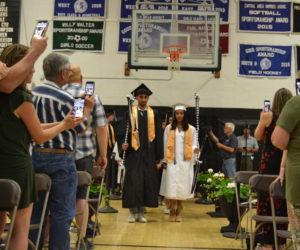 Class Marshals Ralph Zoorob and Issabella Herring lead the Lincoln Academy Class of 2023 to their seats in the Nelson Bailey Gymnasium on Friday, June 2. Family and friends stand to welcome them into the gym and capture the moment on their phones. (Johnathan Riley photo)