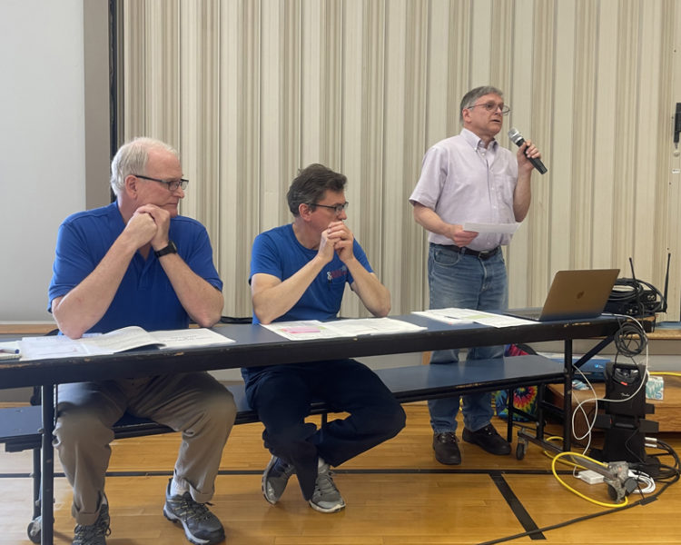 Somerville Select Board Chair Chris Johnson addresses the annual town meeting held in Somerville Elementary School gymnasium on Saturday, June 24. From left: select board members Donald Whitmer-Kean, Don Chase, and Johnson. (Sherwood Olin photo)