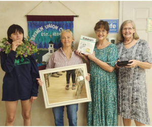 From left: Ireland Teele displays a wreath and samples one of the locally made pastries; Barbara Caggini displays a framed mirror, Joan Teele shows a kitchen appliance, and Janet Leonard holds the rest of the cookies. (Photo courtesy Bremen Union Church)