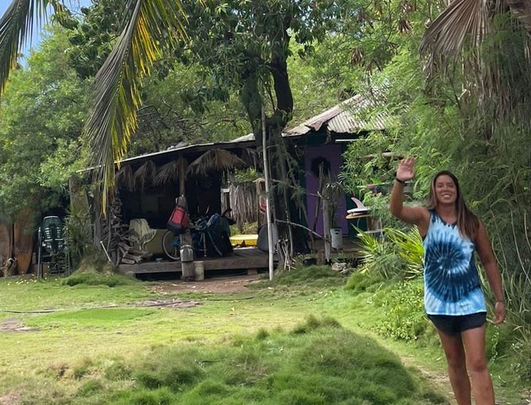 Emma Lazzari waves in front of her house in Lahaina, Hawaii in a photo taken before the Aug. 8 wildfires. Lazzari said her house was near popular surf spots and friends would often park there to get access to the beach. (Photo courtesy Emma Lazzari)