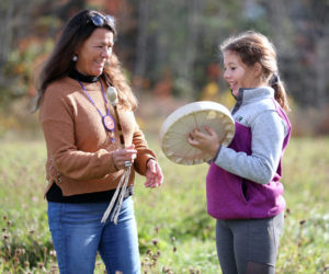 Passamaquoddy educator Sandra Bassett invites a student from the Jefferson Village School to try out a traditional drum. (Photo courtesy Coastal Rivers Conservation Trust)