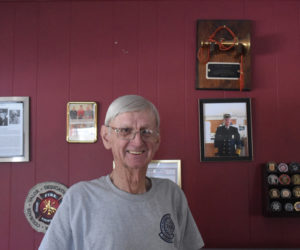 Jim Hall stands at home in Damariscotta with a wall displaying accomplishments from over 60 years of fire department service and decades of involvement with his hometown. "I just like to keep going," said Hall, who keeps busy at Colby and Gale Inc. - formal retirement in 2007 notwithstanding - and with the Damariscotta Fire Department, where he serves as deputy chief. (Elizabeth Walztoni photo)