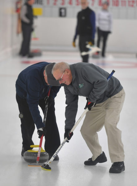 Teammates Chris Burrough (left) and Kevin Connolly sweep the ice to curl a stone at the Belfast Curling Club. (Mic LeBel photo)