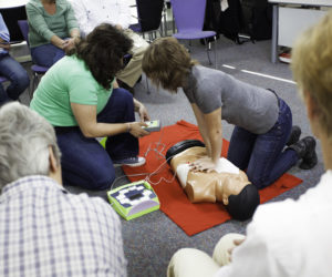 Female instructors demonstrate chest compressions on a CPR dummy with a defibrillator. (Photo courtesy American Heart Association)