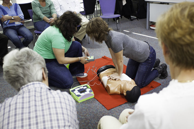 Female instructors demonstrate chest compressions on a CPR dummy with a defibrillator. (Photo courtesy American Heart Association)