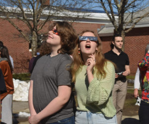 Lincoln Academy freshmen Sawyer Ruit and Fiona Duffy look up at the eclipse after school on Monday, April 8. Event organizer Laura Phelps, the school's librarian, said student excitement for the event was heartening. (Elizbaeth Walztoni photo)