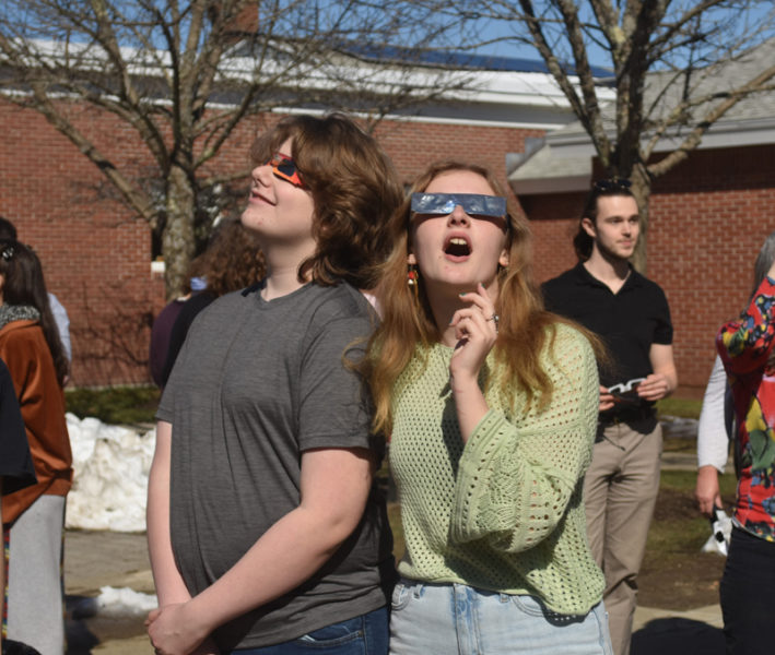 Lincoln Academy freshmen Sawyer Ruit and Fiona Duffy look up at the eclipse after school on Monday, April 8. Event organizer Laura Phelps, the school's librarian, said student excitement for the event was heartening. (Elizbaeth Walztoni photo)