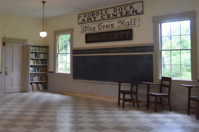 Different signs from the Village School at Puddle Dock's past hang from the wall in Alna on Tuesday, July 30. The building has acted as a school, town office, art center, and it is currently available as a rentable space. (Nolan Wilkinson photo)