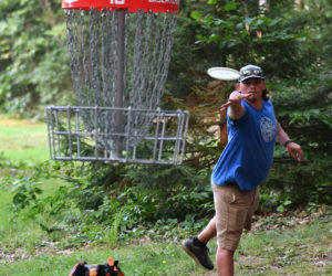 Keegan Dunican tosses his disc into the hanging basket at the 10th hole of the Cider Hill Farm disc golf course in Waldoboro during random doubles league play on Aug. 13. (Mic LeBel photo)