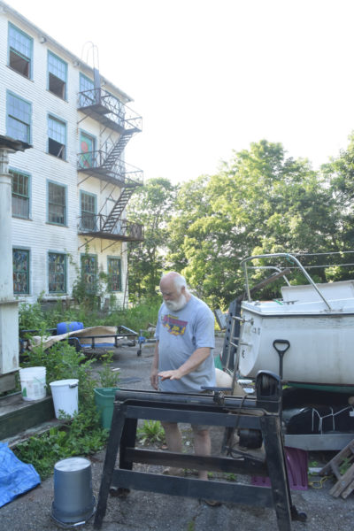 Bobo Hachmeister, of Waldoboro, gestures to a lathe set up outside the former Paragon button factory, where he has lived for 27 years. Hachmeister is a woodworker and artist who enjoys restoring boats and old buildings. (Molly Rains photo)