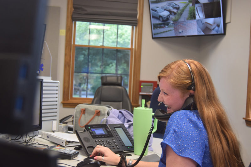 Rhiannon "Rhi" Hersey laughs at a joke told by fellow dispatcher Regan Pearce while on a nonemergency line on the phone at the Lincoln County Communications Center in Wiscasset on Thursday, July 25. Hersey, who is the most experienced of the three dispatchers on the shift, takes on the role of acting supervisor. (Nolan Wilkinson photo)