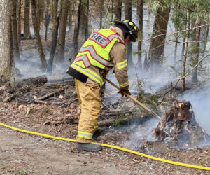 A firefighter rakes over a fire on Cove Lane in Damariscotta on Tuesday, Nov. 12. Damariscotta Fire Chief John Roberts said the blaze started when the wind pushed a power line up against a tree repeatedly until it caught fire. (Johnathan Riley photo)