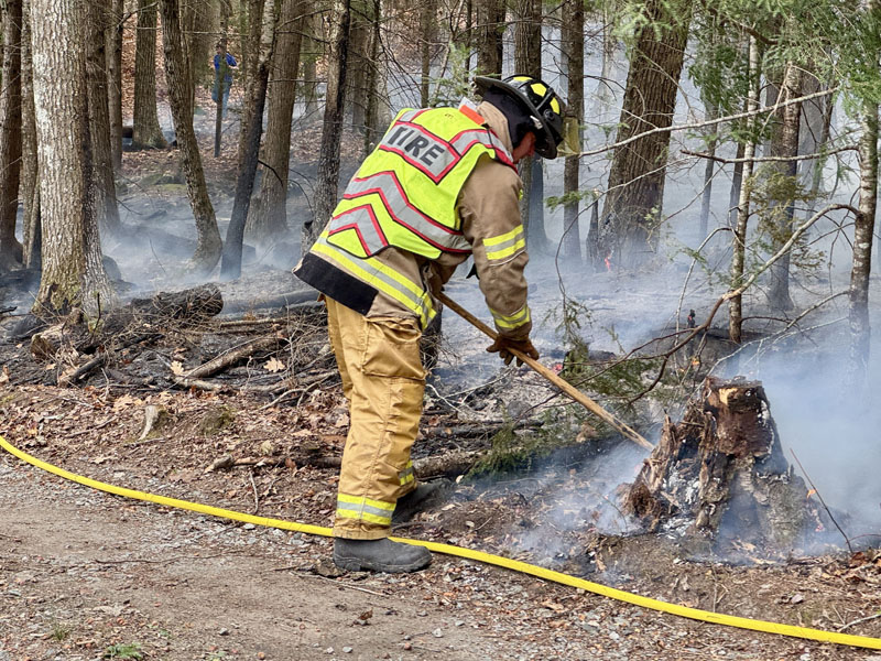 A firefighter rakes over a fire on Cove Lane in Damariscotta on Tuesday, Nov. 12. Damariscotta Fire Chief John Roberts said the blaze started when the wind pushed a power line up against a tree repeatedly until it caught fire. (Johnathan Riley photo)