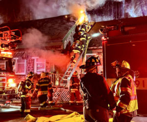 Firefighters converse while others scale a ladder to the roof of the structure located at 268 Jefferson St. in Waldoboro on Sunday, Nov. 17. (Johnathan Riley photo)