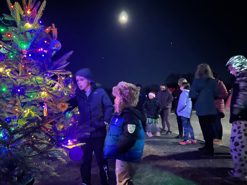 Gavin Wright (left), 10, and Winston Johnson, 4, both of Edgecomb, watch as a Charlie Brown Christmas tree is lit aglow outside Edgecomb Eddy School the evening of Friday, Dec. 13. Each class at the school decorated one of the trees, which were provided at a discount by Green Acre Christmas Tree Farm, of Edgecomb, and purchased by former Edgecomb Select Board Chair Mike Smith. (Molly Rains photo)