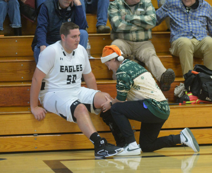 Lincoln Academy athletic trainer Megan Day evaluates Tyson Ball's knee during halftime. (Paula Roberts photo)