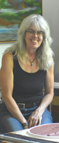 Sculptor Daphne Pulsifer laughs at a work station inside her studio on Light House Road on the island of Monhegan. Pulsifer and her husband raised small children on the island, and she has shaped her identity as a sculptor amidst the community of artists there, she said. (Molly Rains photo)