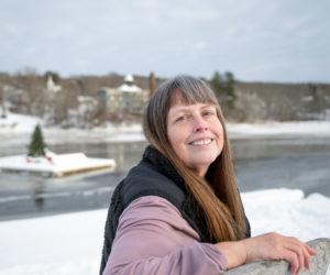 Rebecca Smith Waddell smiles from a stone bench at the snow-covered Pine Street Landing in Waldoboro on Saturday, Dec. 27. Behind her the towns floating Christmas tree is hemmed in by ice on the Medomak River. (Bisi Cameron Yee photo)