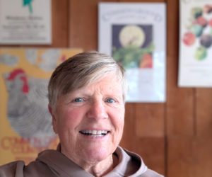 Lisa Miller stands in front of a collection of posters advertising several years of the Common Ground Fair in her Somerville home. A public health consultant, Miller moved to Maine in 1977 where she launched a career, raised a family, and served three terms in the Maine House of Representatives, among other things. (Sherwood Olin photo)