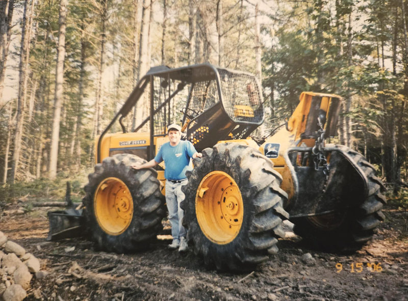 David Trahan stands next to one of two skidders he used in his logging business. While he has little time for his own business now, both skidders are still operational and ready to go to work, Trahan said. (Courtesy photo)