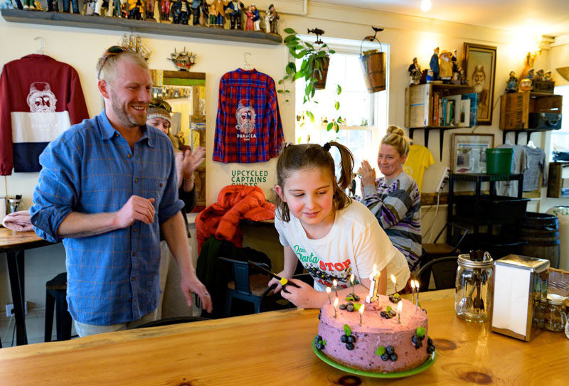 Olive Ackerman (center) lights a birthday cake while Chauncey Erskine looks on at Panacea in Wiscasset on Sunday, Feb. 1. Olive made the blueberry lemon cake with mom Lucy Oyster. I got to lick the whole whisk! she said. (Bisi Cameron Yee photo)