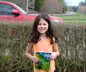 Addisyn Griffin smiles with this years annual report featuring her artwork on the cover. Addisyn, a second grade student at Edgecomb Eddy School, said her favorite subject is art. (Emily Bracher photo)
