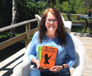 Allison Keeton holds the first two books in her Midcoast Maine Mystery series while sitting on the porch of her Pemaquid home. The third book in the series will be released in early 2027, and at least three more are in the works. Keeton uses her experiences and the people around her to help shape what she writes. (Christine Simmonds photo)