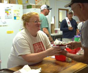 Holly Morgan hands a newly assembled strawberry shortcake to a Strawberry Festival attendee at St. Philips Episcopal Church in Wiscasset on Saturday, June 27. In the kitchen, a team formed an assembly line to create the dessert. (Lily Wasserman photo)