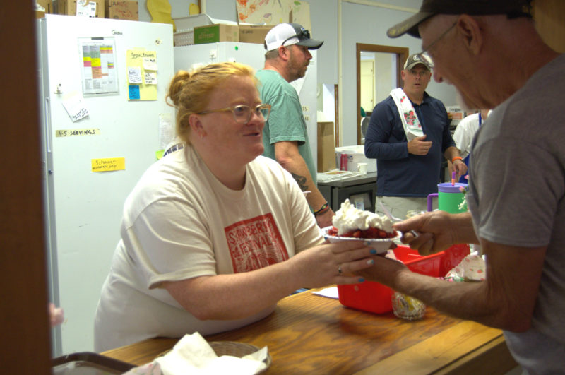 Holly Morgan hands a newly assembled strawberry shortcake to a Strawberry Festival attendee at St. Philips Episcopal Church in Wiscasset on Saturday, June 27. In the kitchen, a team formed an assembly line to create the dessert. (Lily Wasserman photo)