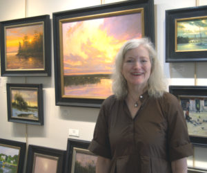Sylvan Gallery director Ann Scanlan stands in front of some of the works in her Wiscasset gallery on Tuesday, June 30. The gallery is celebrating its 25th anniversary this year. (Lily Wasserman photo)